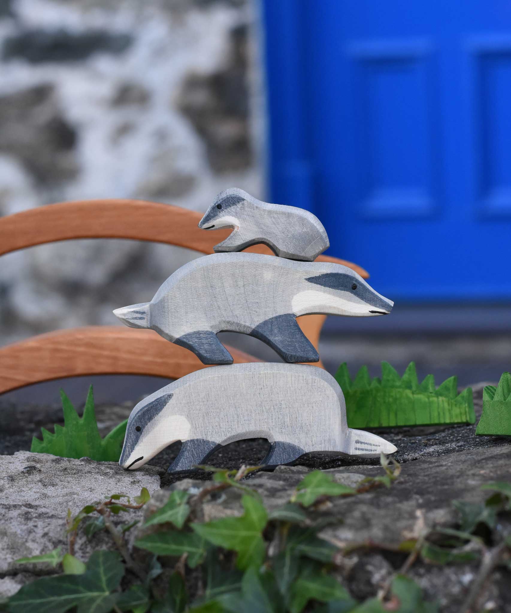 Three Ostheimer wooden badger figures tacked on top of each other on a stone wall outdoors. The badger at the bottom has it's head down the one in the middle  has it's had straight with the small badger placed on the top of the stack.