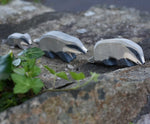 A group of three wooden toy badgers lined up on a stone wall outdoors. The one at the front has it's head down, the one in the middle has it's head straight with the small badger following at the back of the line.  