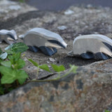 A group of three wooden toy badgers lined up on a stone wall outdoors. The one at the front has it's head down, the one in the middle has it's head straight with the small badger following at the back of the line.  