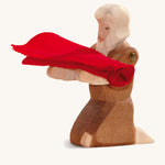 A kneeling wooden beggar figure holding a piece of red cloth on a cream background