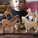 Two Ostheimer colts wooden toy horse figures placed on the back of two larger wooden toy horses. Child can be seen looking on on the background. 