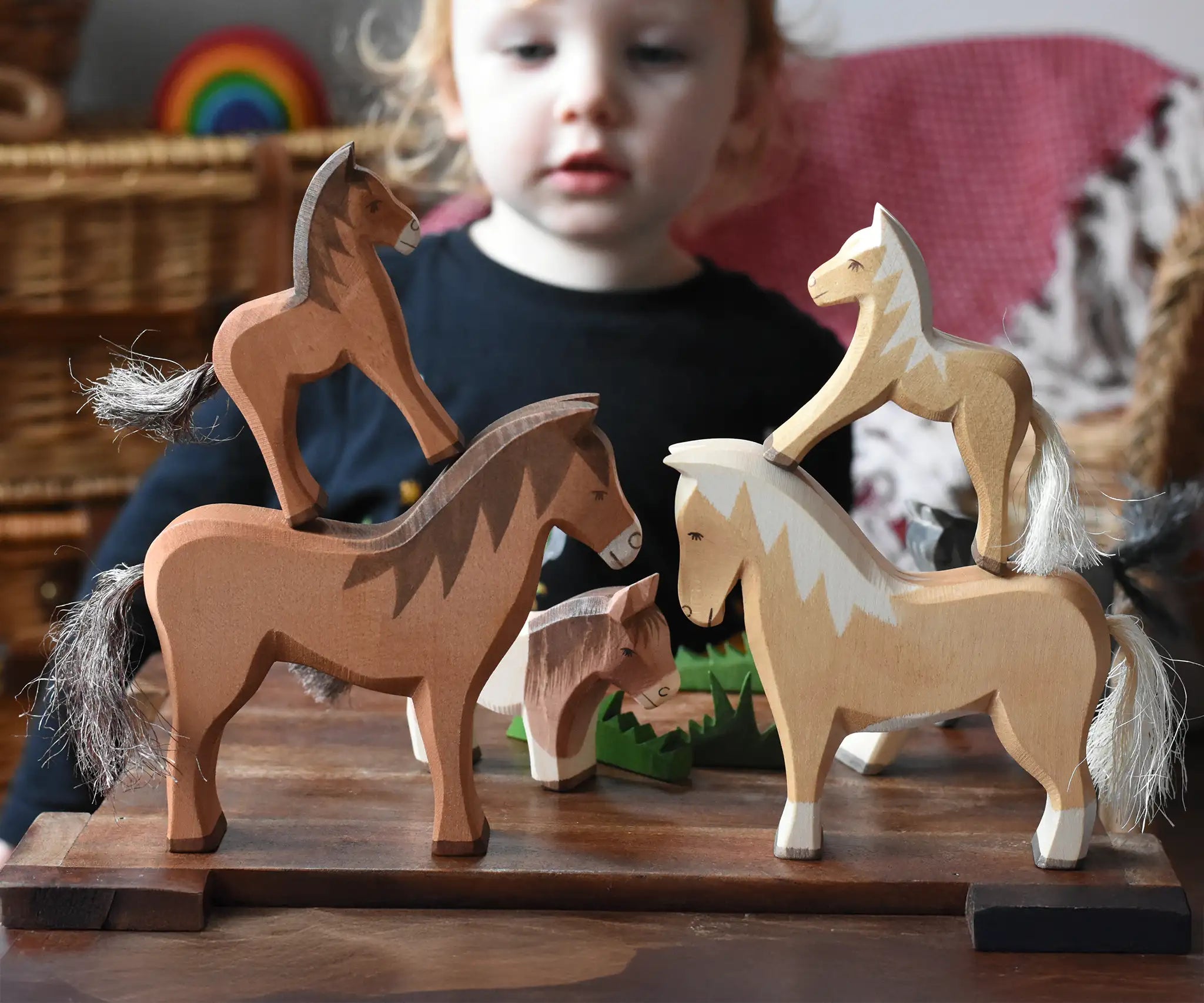 Two Ostheimer colts wooden toy horse figures placed on the back of two larger wooden toy horses. Child can be seen looking on on the background. 
