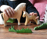 Close up of a child's hand playing with Ostheimer haflinger horse and colt wooden toy figures. 
