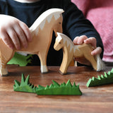 Close up of a child's hand playing with Ostheimer haflinger horse and colt wooden toy figures. 