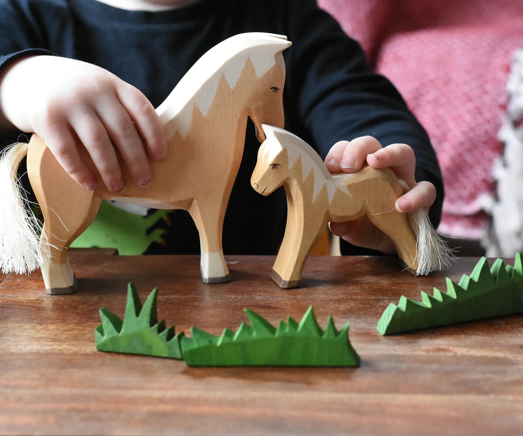 Close up of a child's hand playing with Ostheimer haflinger horse and colt wooden toy figures. 