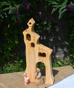 An Ostheimer wooden bell tower placed on a small table outdoors. These wooden figures are part of a large range of expertly hand crafted, Waldorf inspired, wooden toys here at Babipur.