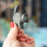 An Ostheimer hand made and hand painted wooden black cat figure  held in an adult's hand. These wooden figures are part of a wide range of expertly hand crafted wooden toys here at Babipur. 