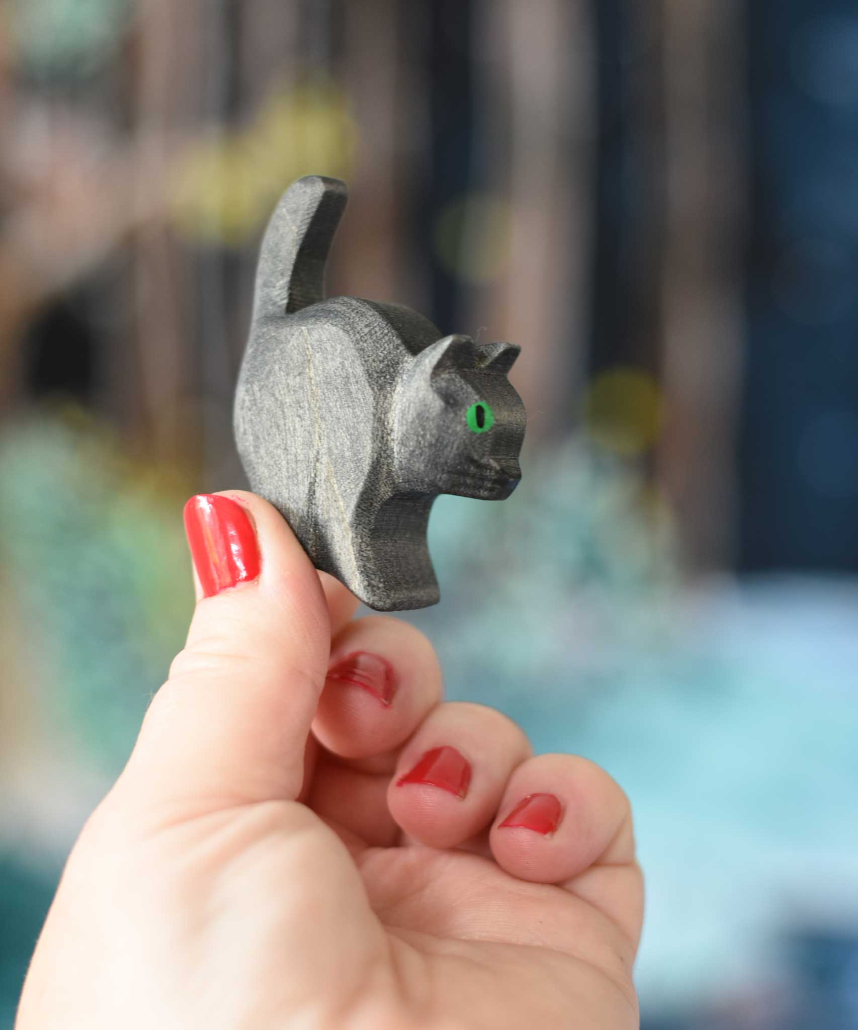 An Ostheimer hand made and hand painted wooden black cat figure  held in an adult's hand. These wooden figures are part of a wide range of expertly hand crafted wooden toys here at Babipur. 