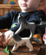 Child playing with Ostheimer wooden horses stacking a black colt figure on top of a running Shetland. 