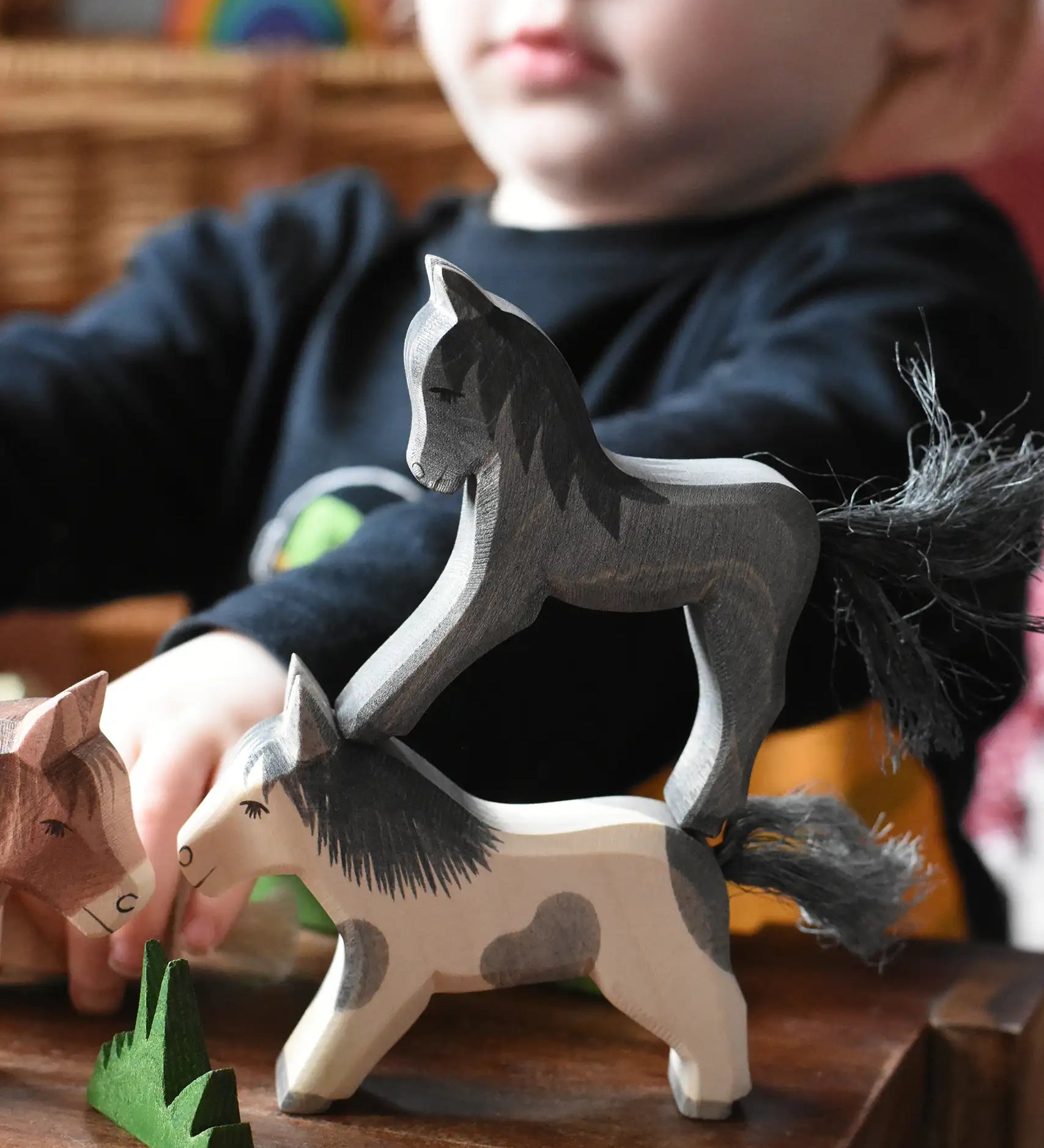 Child playing with Ostheimer wooden horses stacking a black colt figure on top of a running Shetland. 