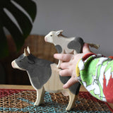 Child playing with Ostheimer black and white wooden toy animal figures. The child has placed a calf on the back of a cow.