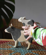 Child playing with Ostheimer black and white wooden toy animal figures. The child has placed a calf on the back of a cow.