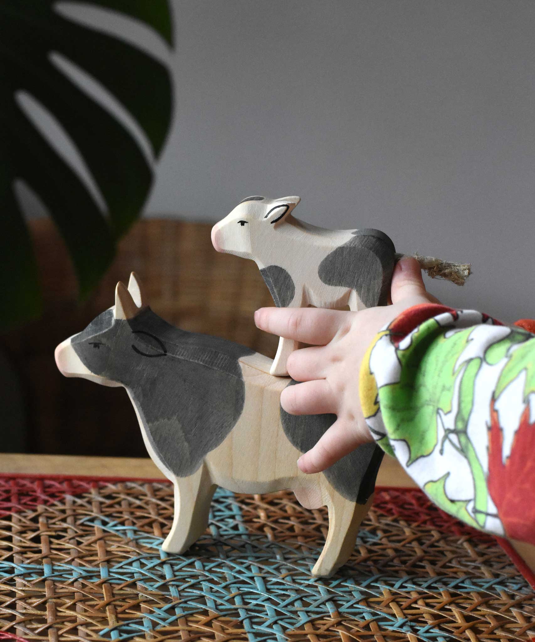 Child playing with Ostheimer black and white wooden toy animal figures. The child has placed a calf on the back of a cow.