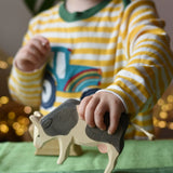 Ostheimer black and white cow eating wooden toy figure in a child's hand being lifted off the green cotton play cloths placed underneath.