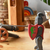 Ostheimer black riding knight handmade wooden toy figure with shield and long sword placed at the front of a small world play scene with castle pieces and a cannon in the background.