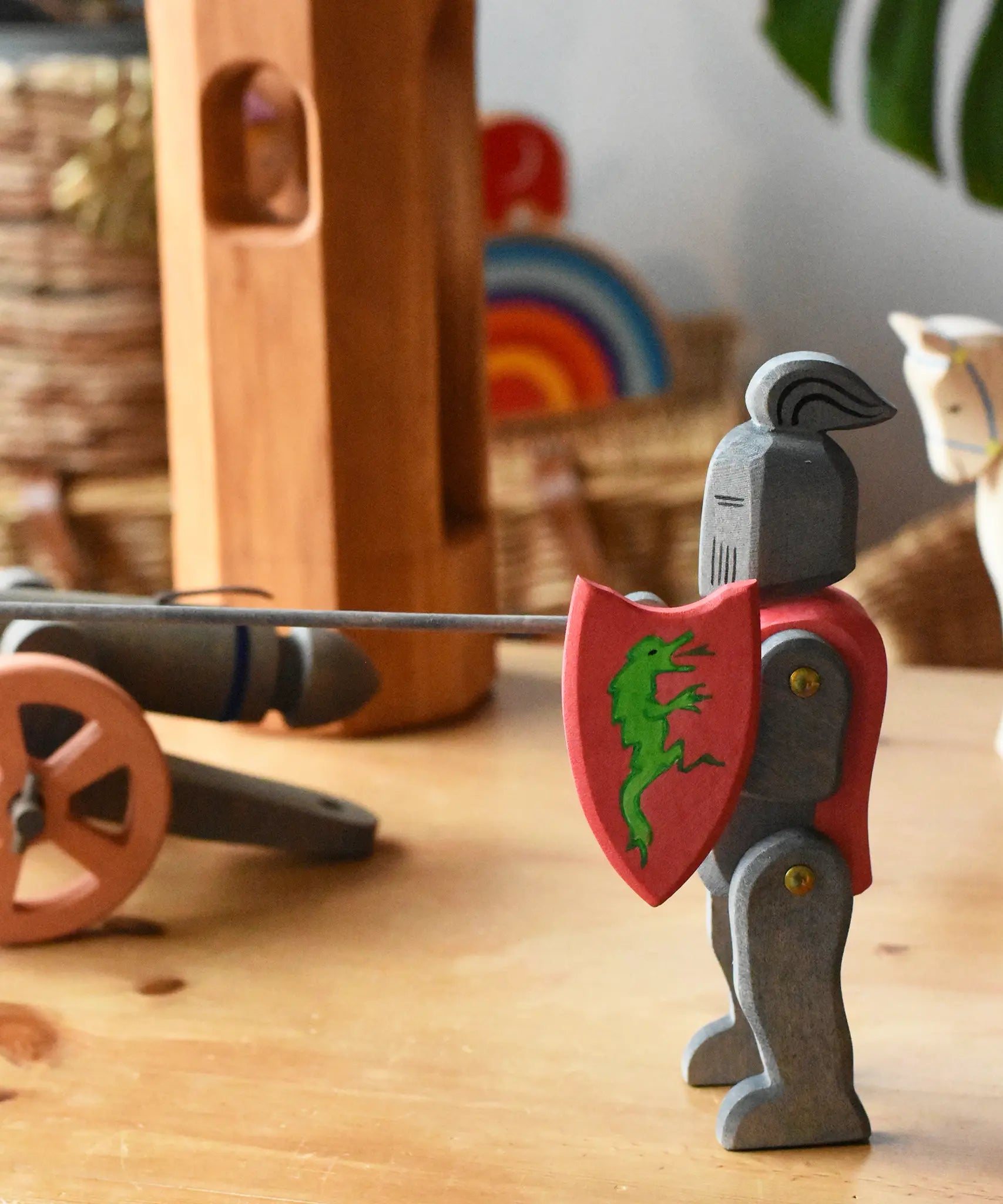 Ostheimer black riding knight handmade wooden toy figure with shield and long sword placed at the front of a small world play scene with castle pieces and a cannon in the background.
