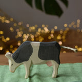 Ostheimer black and white cow eating wooden toy figure placed on a green cotton play cloth.