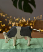 Ostheimer black and white cow eating wooden toy figure placed on a green cotton play cloth.