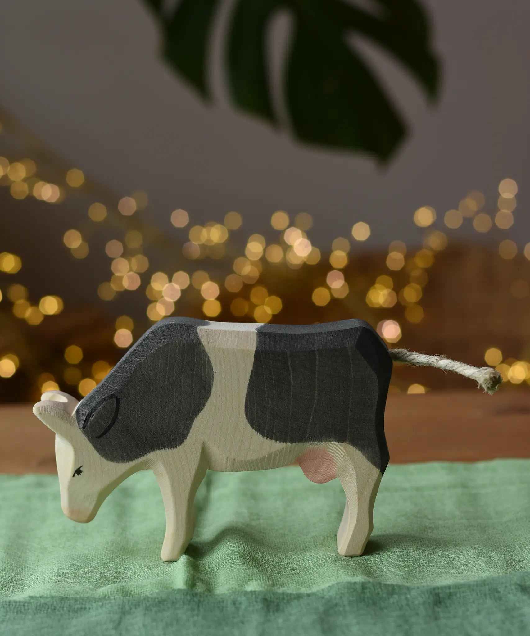 Ostheimer black and white cow eating wooden toy figure placed on a green cotton play cloth.