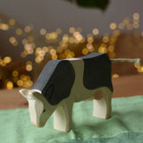 Front of the Ostheimer black and white cow eating wooden toy figure placed on a green cotton play cloth. 