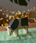 Front of the Ostheimer black and white cow eating wooden toy figure placed on a green cotton play cloth. 