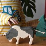 Ostheimer black and white ox wooden toy figure placed on a wooden surface, a child's hand is reaching for it.