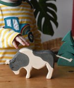 Ostheimer black and white ox wooden toy figure placed on a wooden surface, a child's hand is reaching for it.