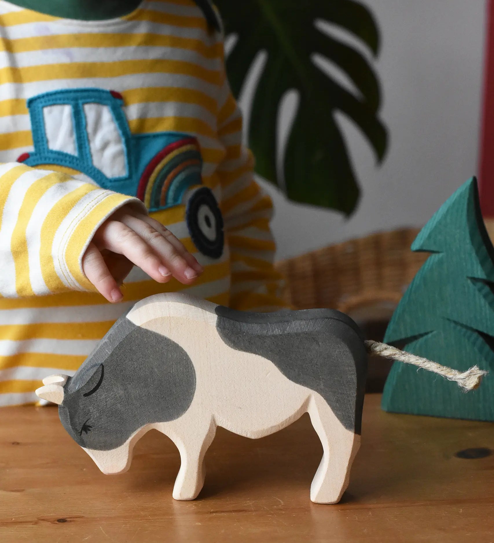 Ostheimer black and white ox wooden toy figure placed on a wooden surface, a child's hand is reaching for it.