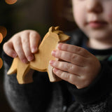 A close up of the Ostheimer collie dog wooden toy figure in a child's hand.  These wooden figures are part of a wide range of expertly hand crafted wooden toys here at Babipur. 