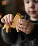 A close up of the Ostheimer collie dog wooden toy figure in a child's hand.  These wooden figures are part of a wide range of expertly hand crafted wooden toys here at Babipur. 