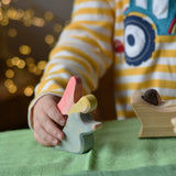 Ostheimer blue kneeling angel wooden toy figure in a child's hand being placed on a green cotton play cloth in a small world play scene.
