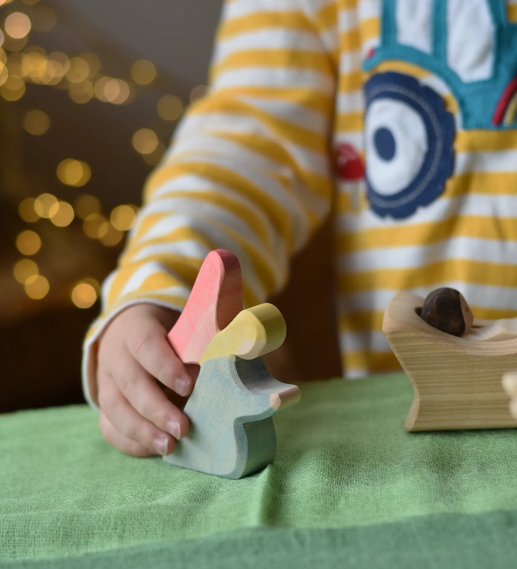 Ostheimer blue kneeling angel wooden toy figure in a child's hand being placed on a green cotton play cloth in a small world play scene.
