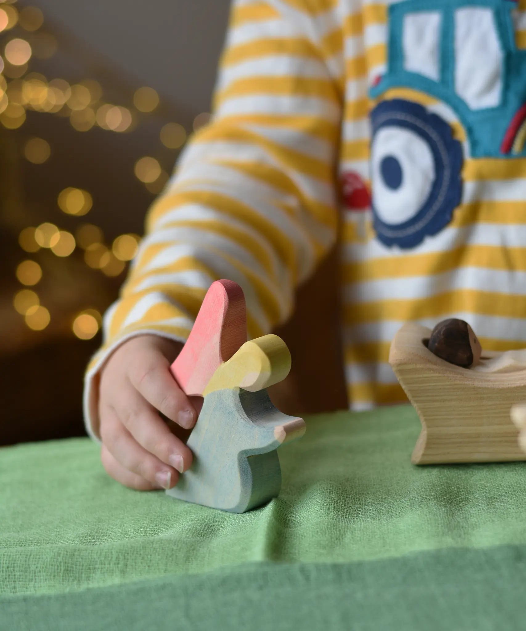 Ostheimer blue kneeling angel wooden toy figure in a child's hand being placed on a green cotton play cloth in a small world play scene.