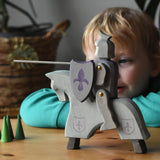 The Ostheimer blue riding wooden knight on a grey horse toy figure placed on a wooden surface with a child looking on in the background. 