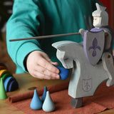Child playing with the Ostheimer blue riding wooden knight on a grey horse toy figure feeding it water Grapat mandala pieces.