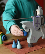 Child playing with the Ostheimer blue riding wooden knight on a grey horse toy figure feeding it water Grapat mandala pieces.