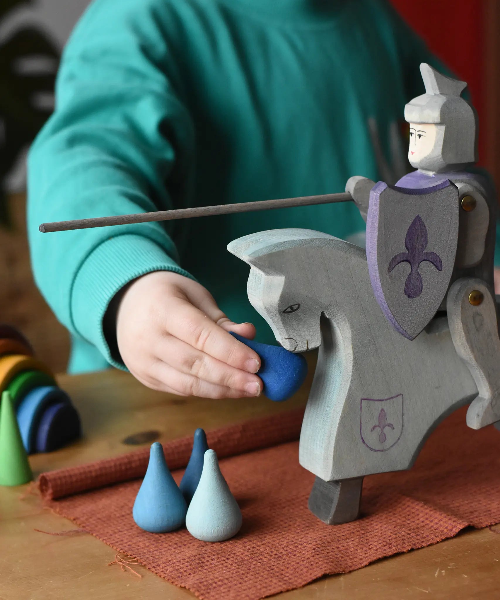 Child playing with the Ostheimer blue riding wooden knight on a grey horse toy figure feeding it water Grapat mandala pieces.