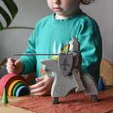 Ostheimer blue riding wooden knight on a grey horse toy figure in a small world play scene with a child in the background.