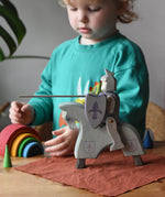 Ostheimer blue riding wooden knight on a grey horse toy figure in a small world play scene with a child in the background.