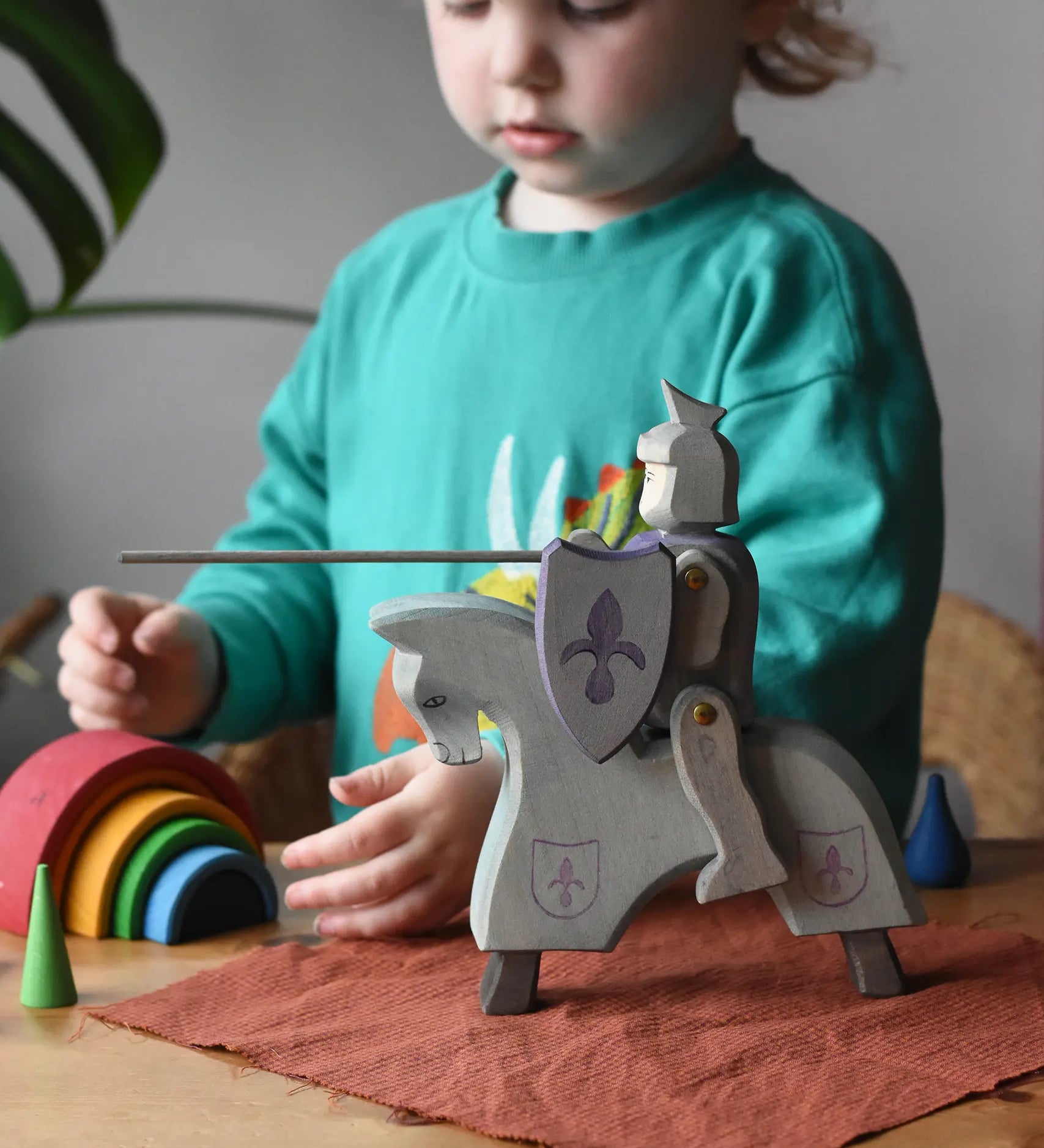 Ostheimer blue riding wooden knight on a grey horse toy figure in a small world play scene with a child in the background.