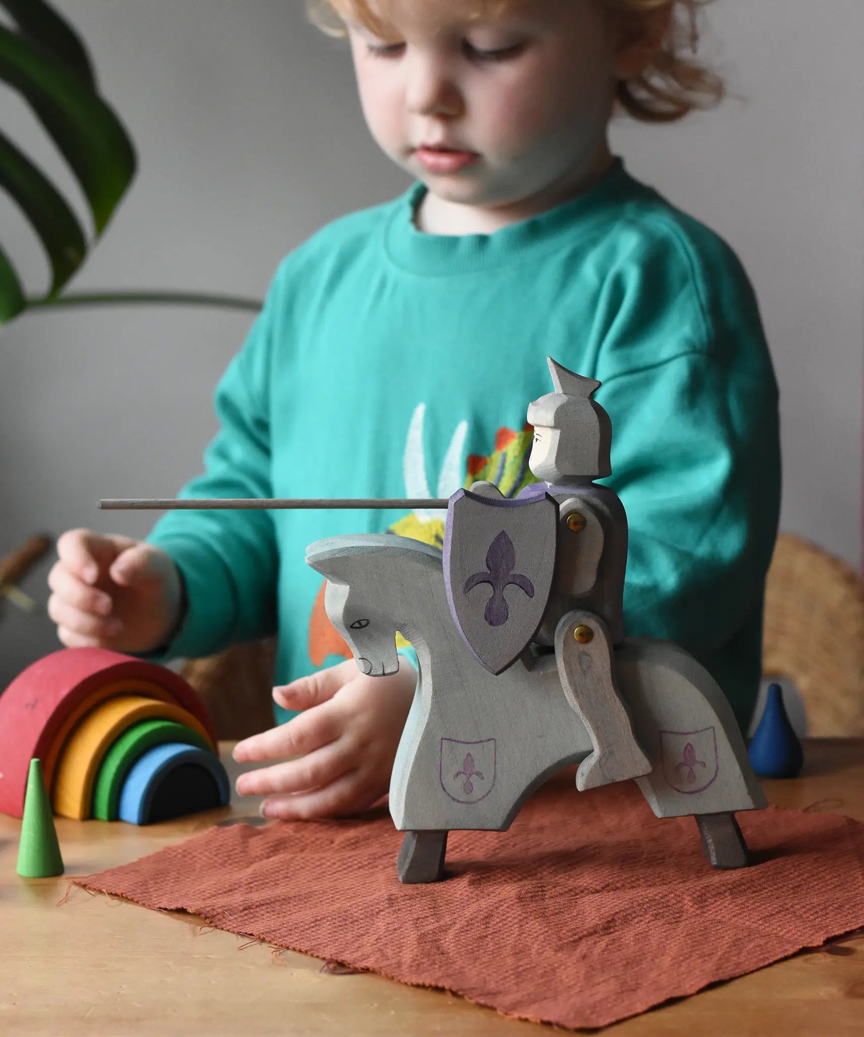 Ostheimer blue riding wooden knight on a grey horse toy figure in a small world play scene with a child in the background.