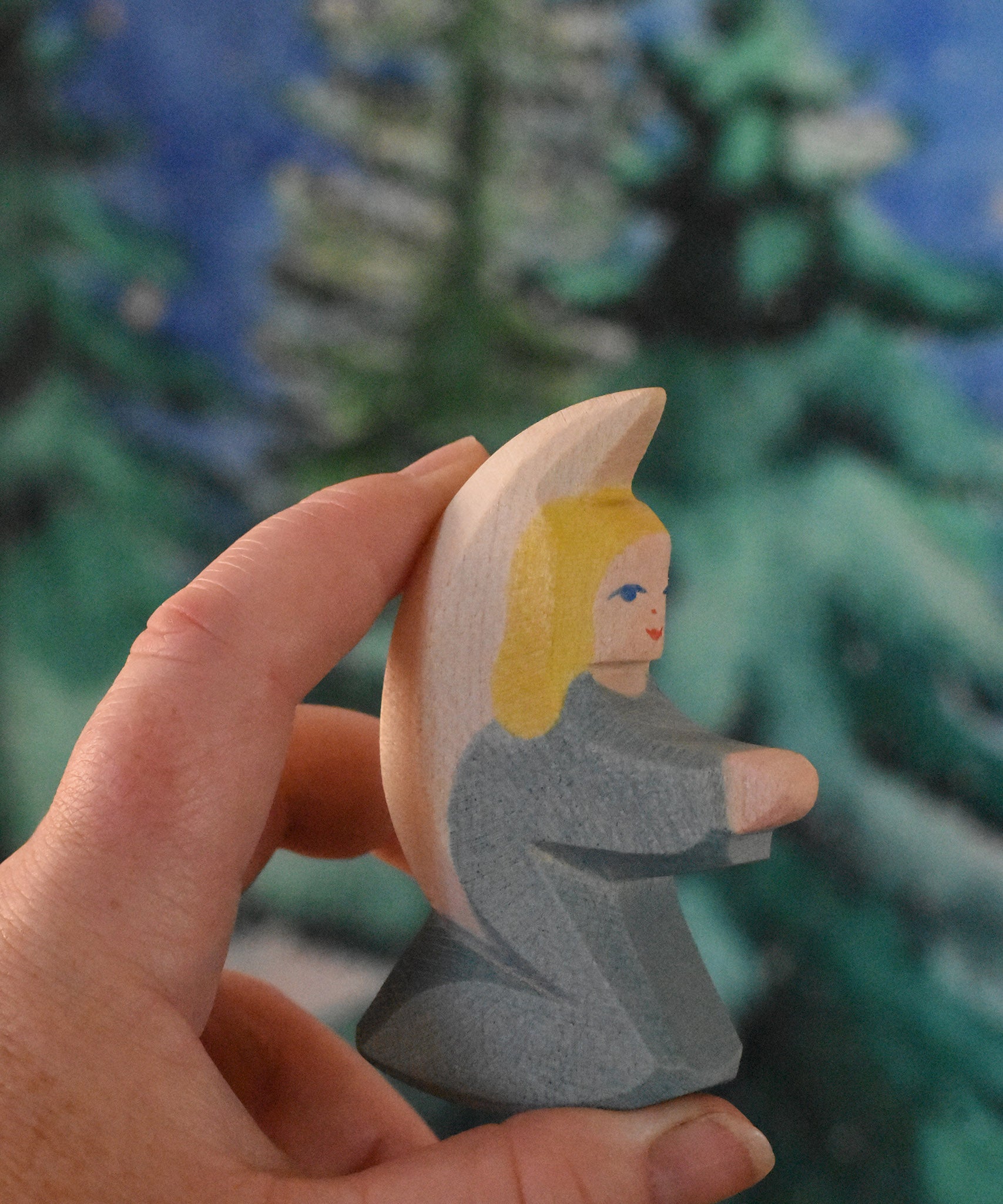 A turquoise blue coloured Ostheimer little angel held in an adult's hand to show scale. This wooden figure is part of a large range of expertly hand crafted, Waldorf inspired, wooden toys here at Babipur. 
