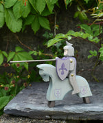 The Ostheimer blue riding wooden knight on a grey horse toy figure placed on a slate surface outdoors.