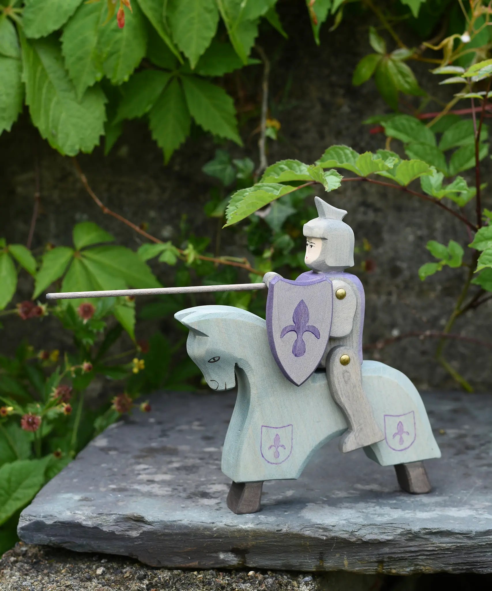 The Ostheimer blue riding wooden knight on a grey horse toy figure placed on a slate surface outdoors.