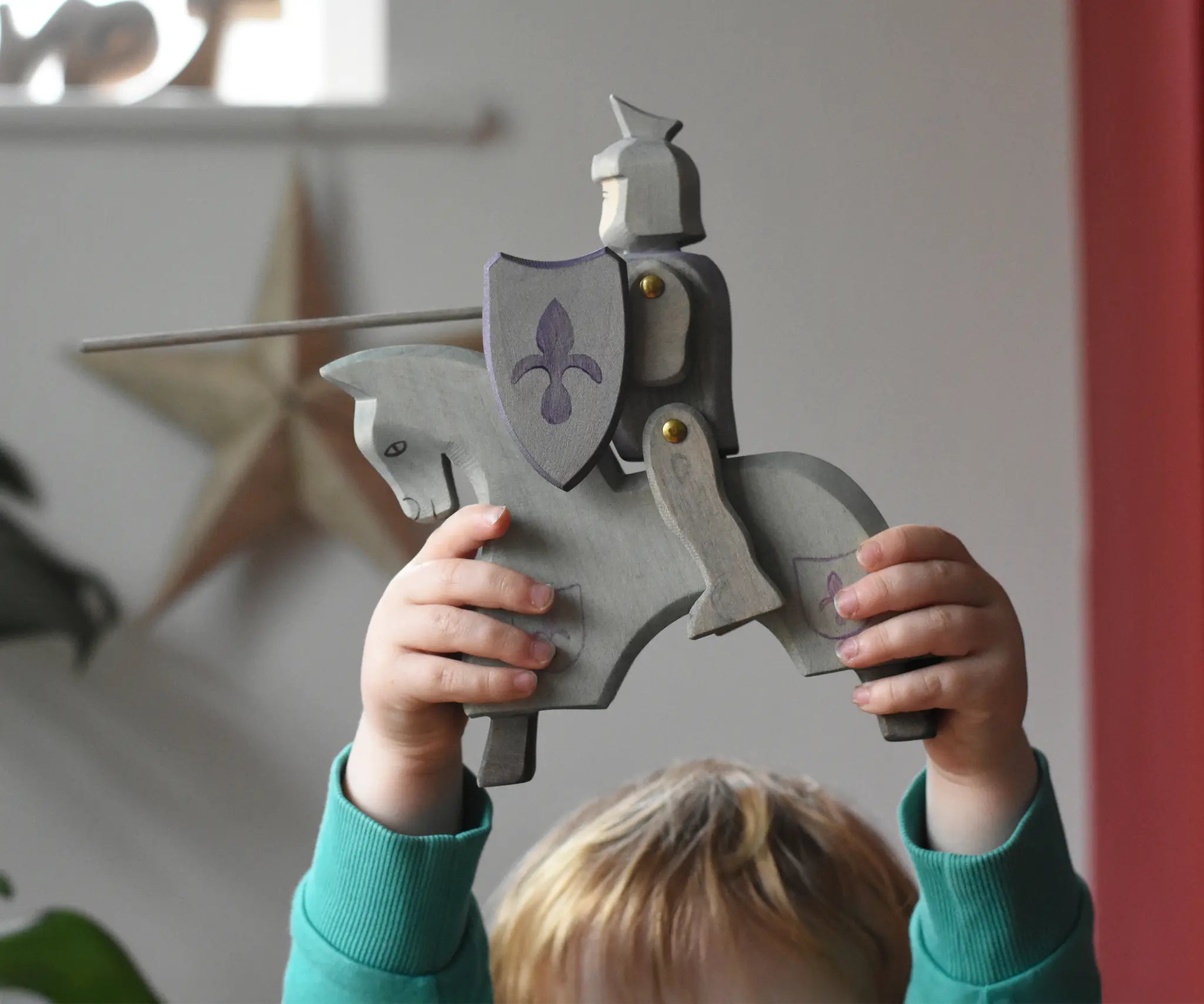 The Ostheimer blue riding wooden knight on a grey horse toy figure held up by a child. 