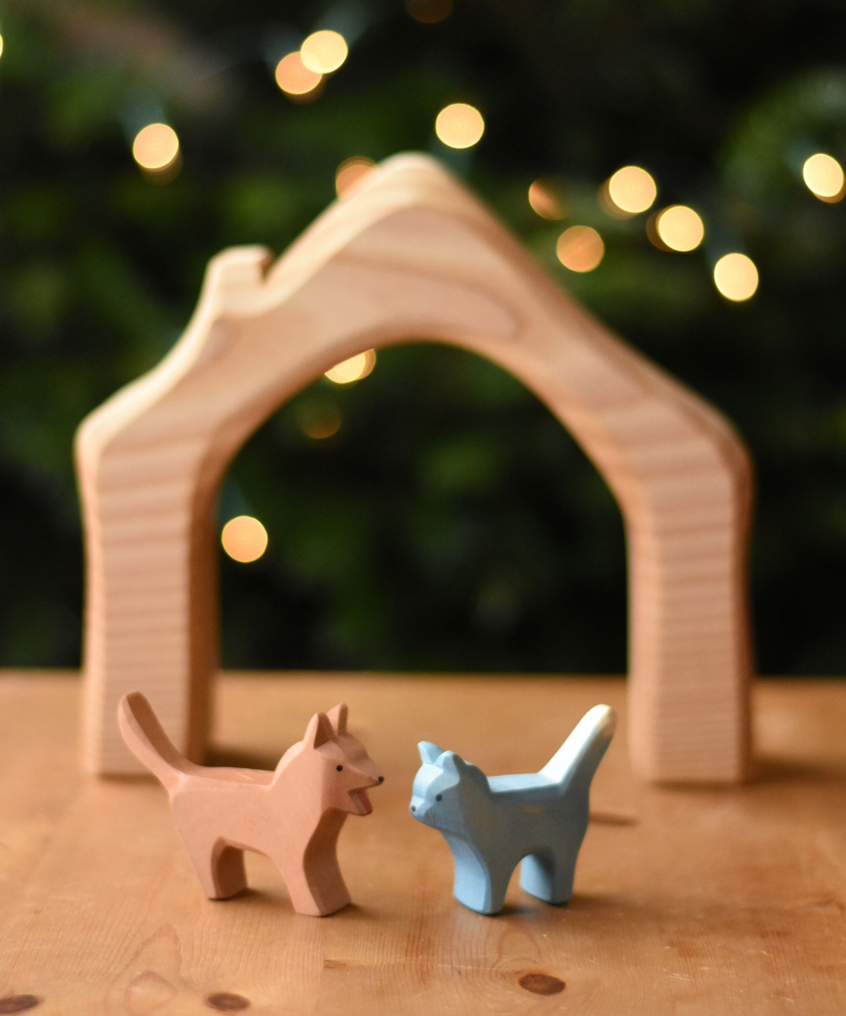 An Ostheimer Bremer dog and cat wooden toy figure placed on a wooden surface with a house shaped wooden piece in the background.  Ostheimer's range of hand crafted, heirloom quality wooden toys are available to buy at Babipur. 