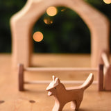 An Ostheimer Bremer dog wooden toy figure placed on a wooden surface with a house shaped wooden piece in the background.  Ostheimer's range of hand crafted, heirloom quality wooden toys are available to buy at Babipur. 