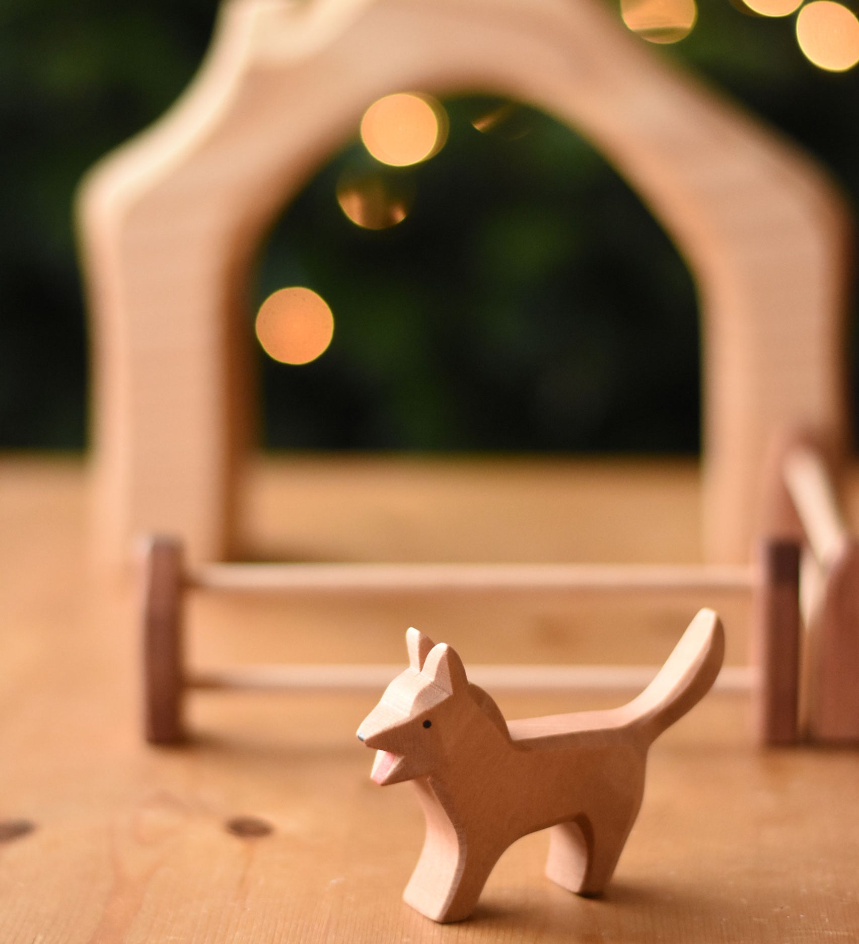 An Ostheimer Bremer dog wooden toy figure placed on a wooden surface with a house shaped wooden piece in the background.  Ostheimer's range of hand crafted, heirloom quality wooden toys are available to buy at Babipur. 