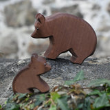 Ostheimer brown bear wooden toy figure placed on a stone wall outdoors with  small sitting bear blurred in the foreground.