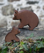 Ostheimer brown bear wooden toy figure placed on a stone wall outdoors with  small sitting bear blurred in the foreground.